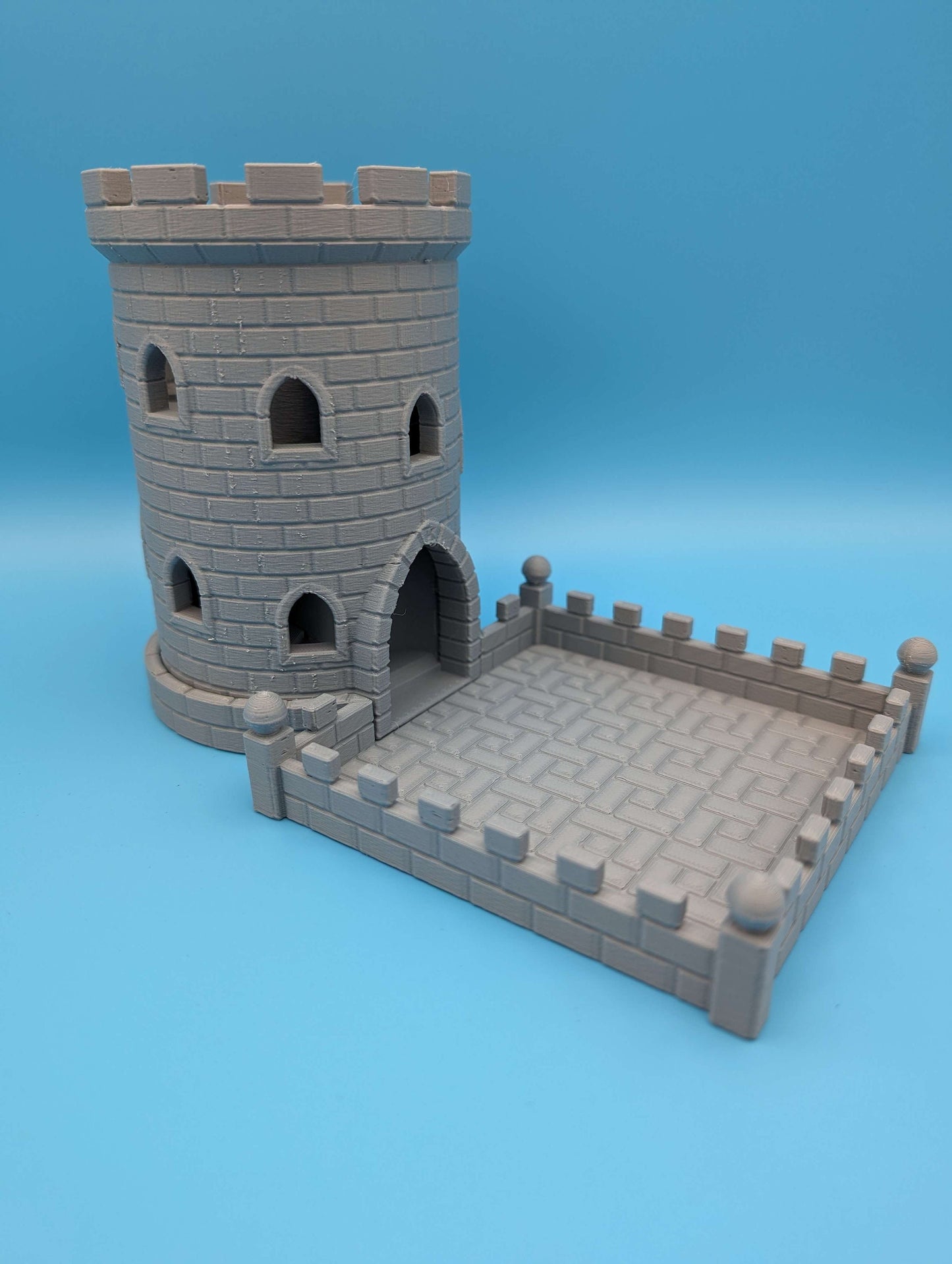 May include: A 3D printed gray tower with a gray brick wall and a gray brick floor. The tower has a small door and several windows. The tower is on a gray brick platform.