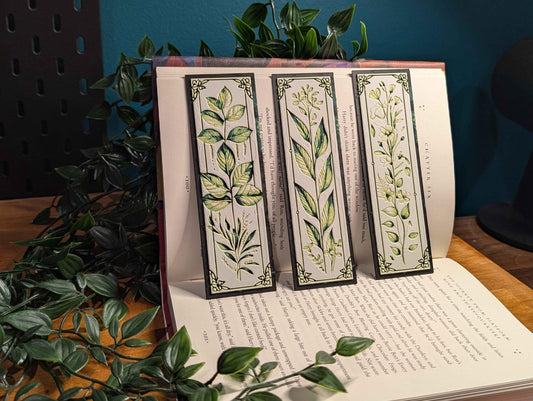 May include: Three botanical bookmarks with dark gray borders and cream-colored backgrounds. Each bookmark features a different illustration of stylized green and yellow plants and a short excerpt of text.  The bookmarks are displayed against a book, partially visible, with text. The overall theme is literary and nature-inspired.